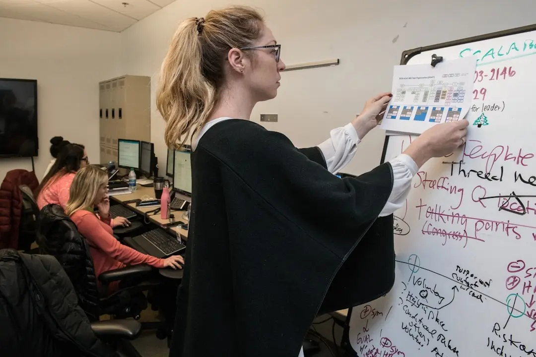 A woman writes on a whiteboard in an office, comparing BA Insight vs Shelf.io solutions.